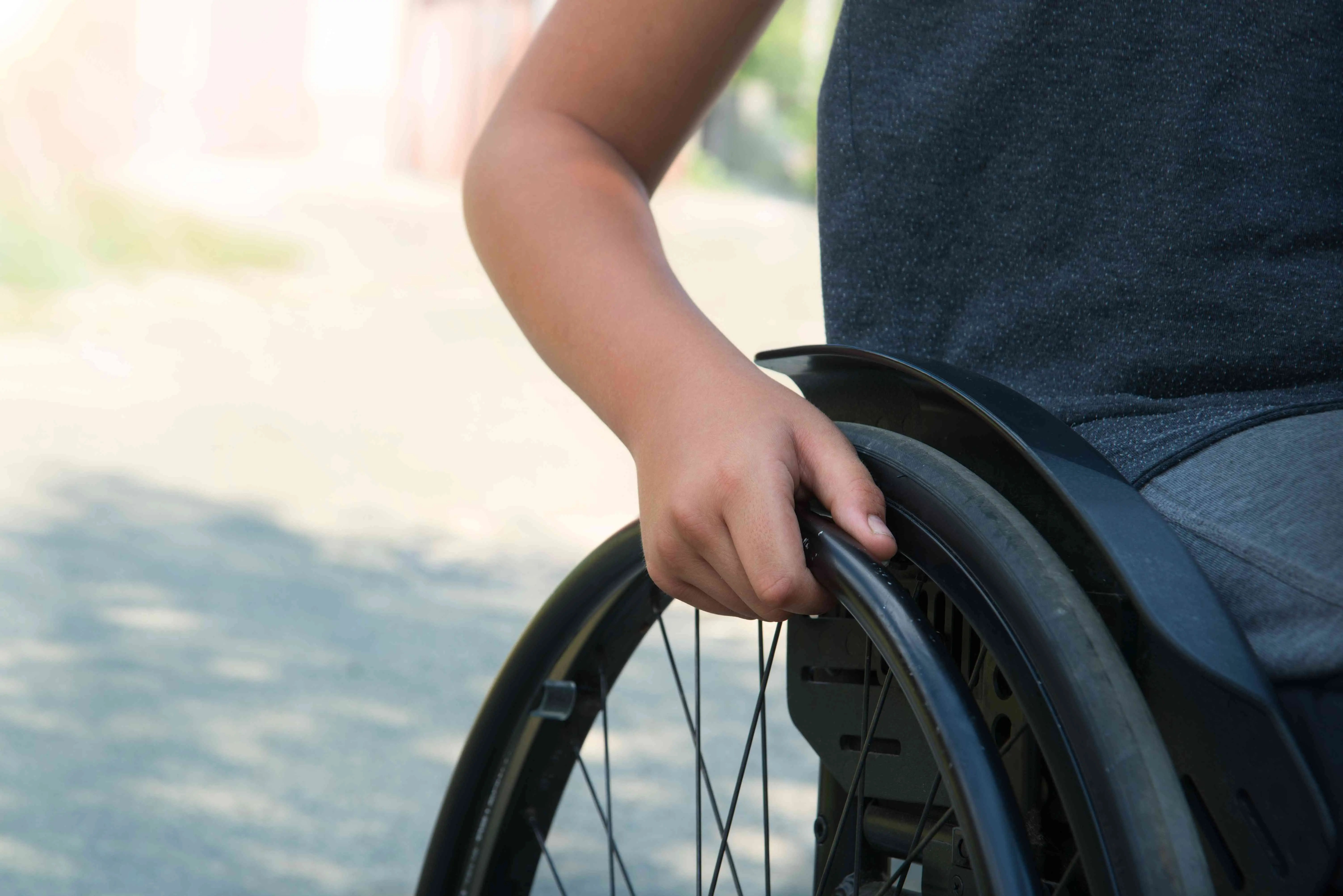 Imagem mostra mão de uma pessoa impulsionando a roda de uma cadeira de rodas ao ar livre.
