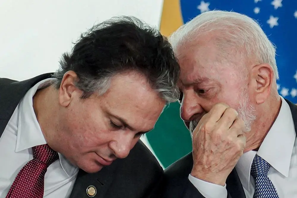 Imagem mostra Camilo Santana e Presidente Lula em conversa próxima, com a bandeira do Brasil desfocada ao fundo.