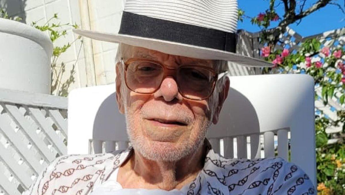 Manoel Carlos usando chapéu branco e óculos de grau. Ele está sentado em uma cadeira.