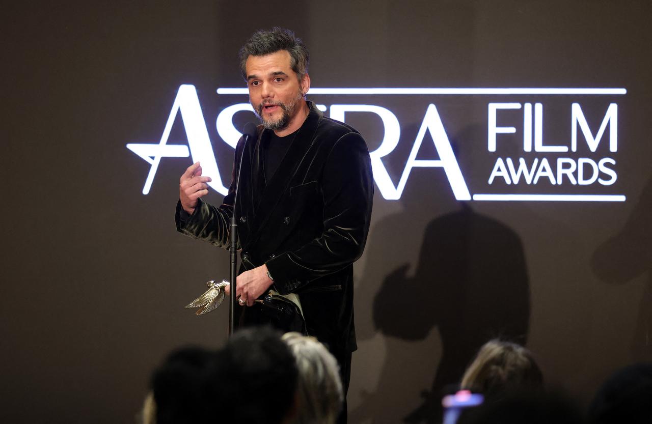 Wagner Moura em terno preto discursando no Astra Awards com uma estatueta na mão.