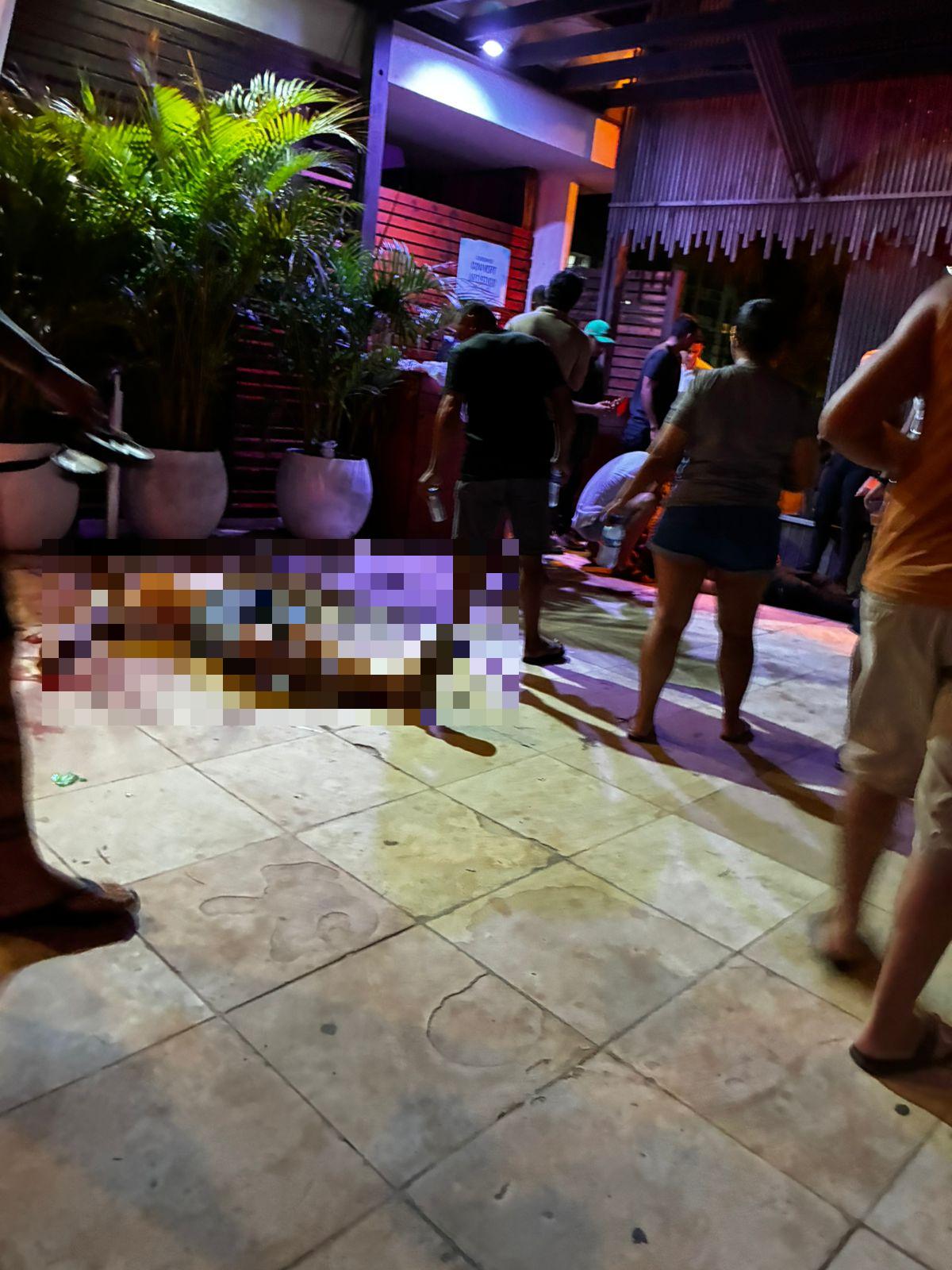 Foto que mostra pessoa caída no chão após homicídio em barraca de praia de Fortaleza. Na foto há diversas pessoas ao redor do corpo.