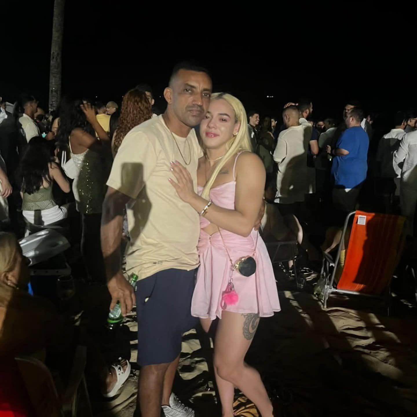 Foto de homem e mulher abraçados em festa com diversas pessoas ao redor.