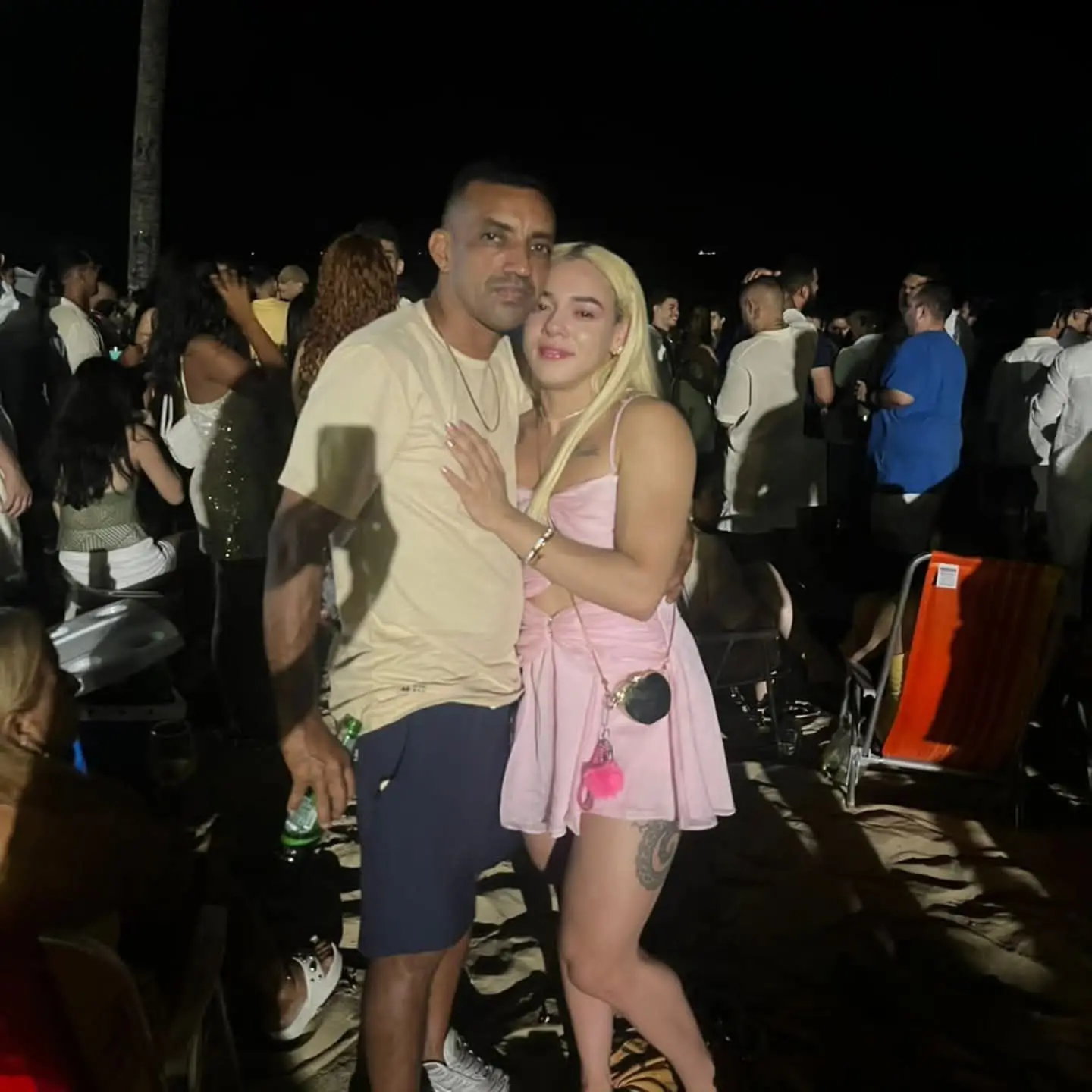 Foto de homem e mulher abraçados em festa com diversas pessoas ao redor.