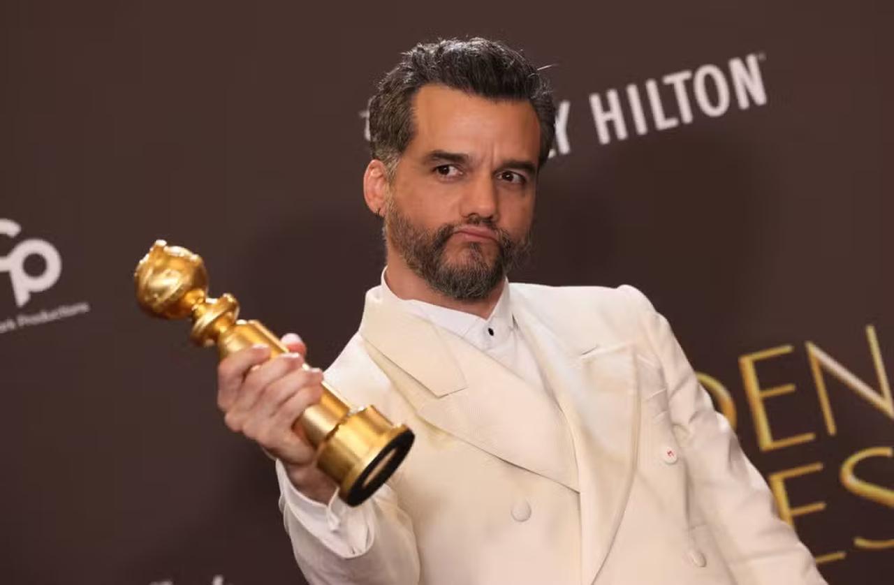 Homem branco de cabelos castanhos e grisalhos e barba castanha, trajando um terno branco e segurando um troféu dourado.