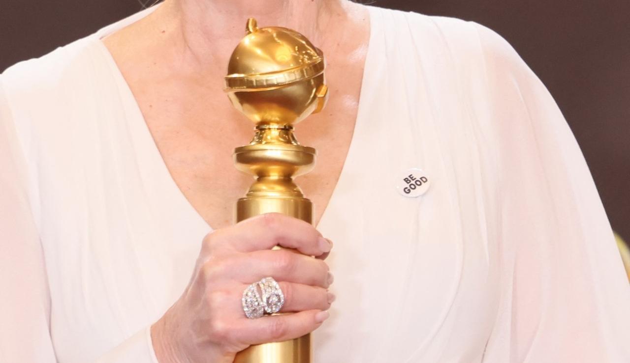 Estatueta dourada do Globo de Ouro, segurada por uma mulher branca com roupa branca. Seu rosto não aparece na foto.