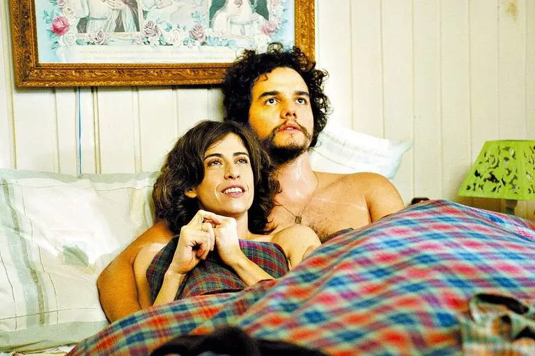 Os atores Fernanda Torres e Wagner Moura aparecem deitados em uma cama sob uma coberta xadrez, em uma cena do filme 