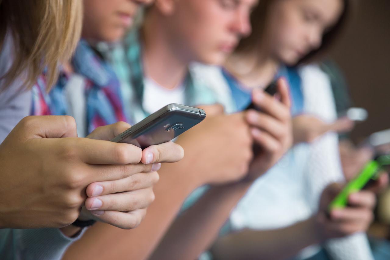 Grupo de jovens concentrados em seus telefones celulares, destacando o uso generalizado de dispositivos móveis entre adolescentes em escolas.