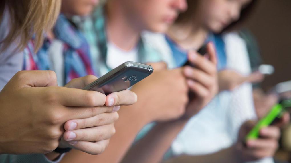 Grupo de jovens concentrados em seus telefones celulares, destacando o uso generalizado de dispositivos móveis entre adolescentes em escolas.