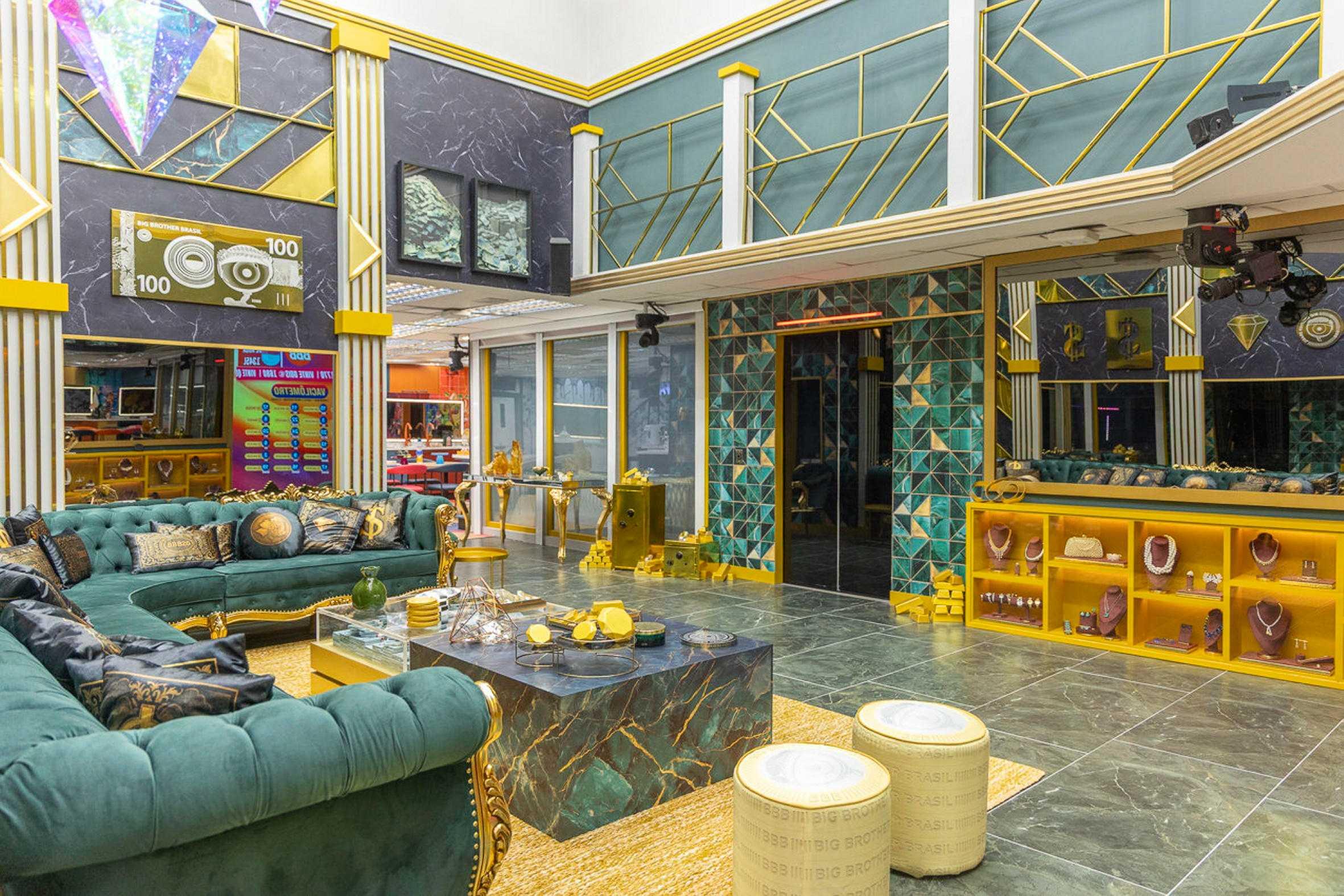 Interior de luxo com tema de riqueza, apresentando um design suntuoso com mobiliário verde e dourado, piso de mármore, expositores de joias e um cofre dourado, característico de um cenário de reality show como o Big Brother Brasil.