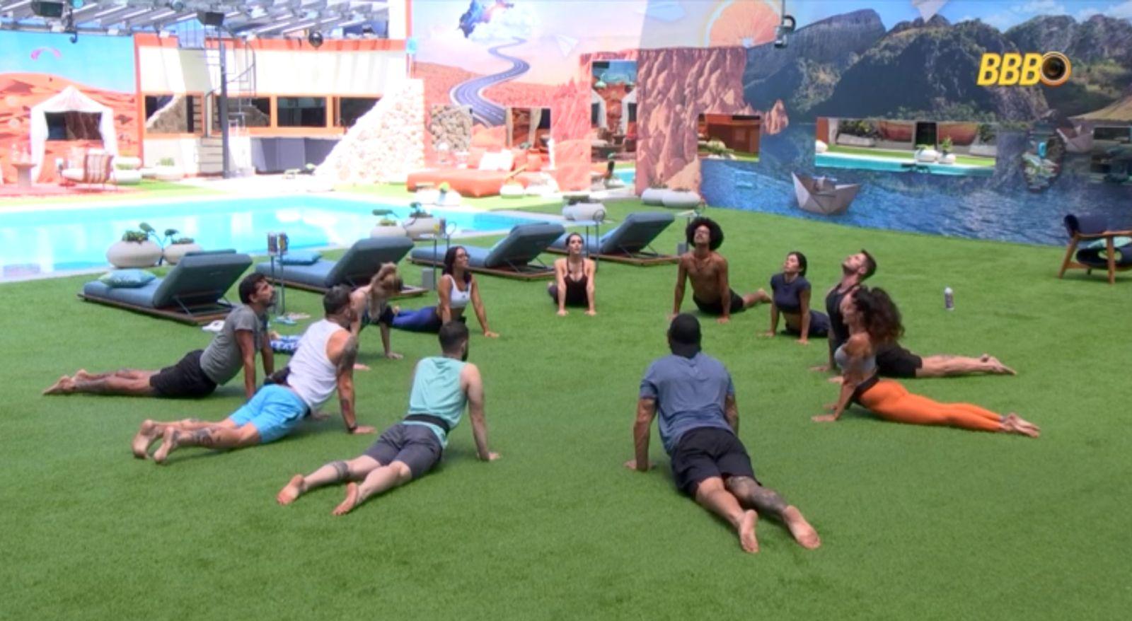 Participantes do BBB praticam ioga no gramado da casa.