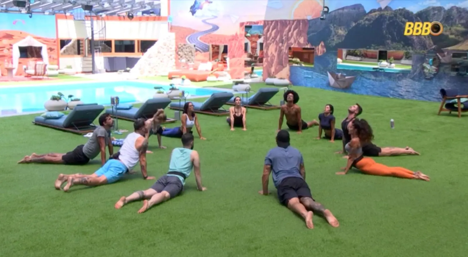Participantes do BBB praticam ioga no gramado da casa.