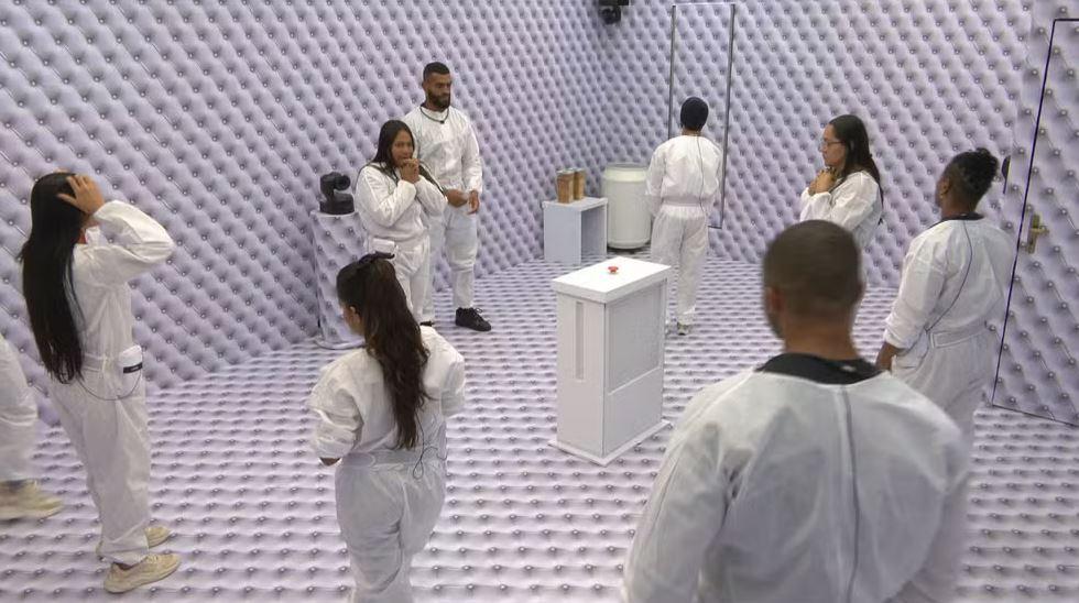Participantes no BBB 26 vestindo macacões brancos em um quarto todo branco.