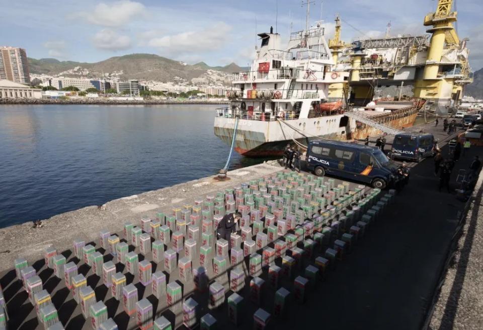 A imagem mostra um navio, próximo a diversos fardos, que continham entorpecentes.