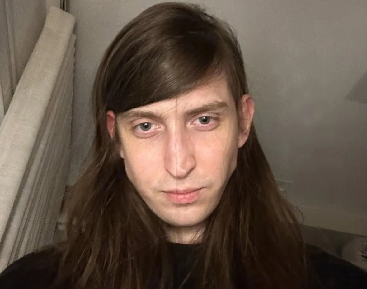 Selfie do influenciador Felca. Na foto, ele, que é jovem, usa camisa preta e está sério. Seu cabelo é castanho, liso e longo e está partido de lado.