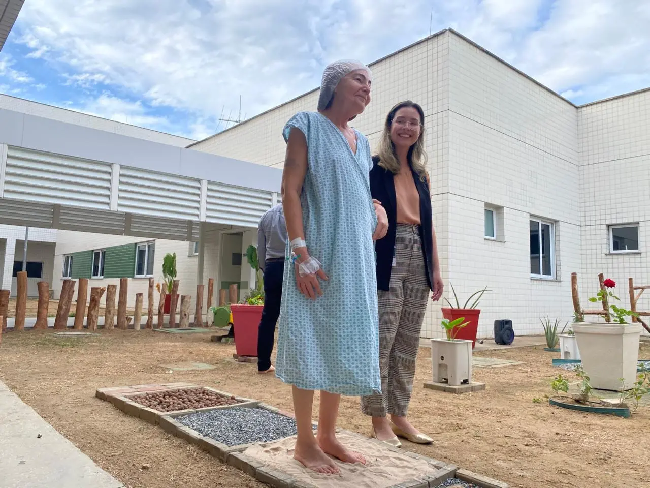 Mulher idosa internada anda sobre areia em jardim sensorial.