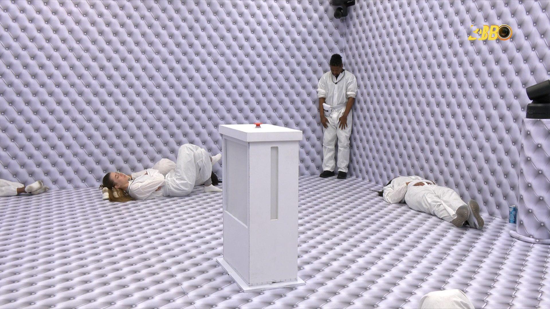 Quarto Branco do BBB 26. Participantes estão deitados no chão, enquanto Leandro encostado na parede.