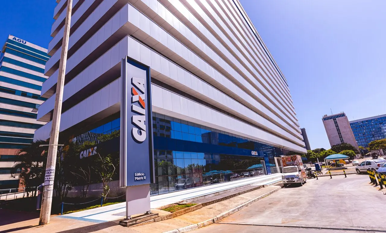Edifício moderno da CAIXA Econômica Federal na cidade, destacando fachada de vidro e arquitetura empresarial, com estacionamento e rua ao redor.