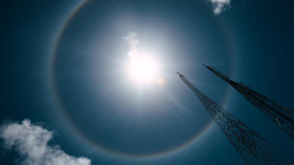 Círculo colorido similar a arco-íris ao redor do sol, com nuvens ao redor.