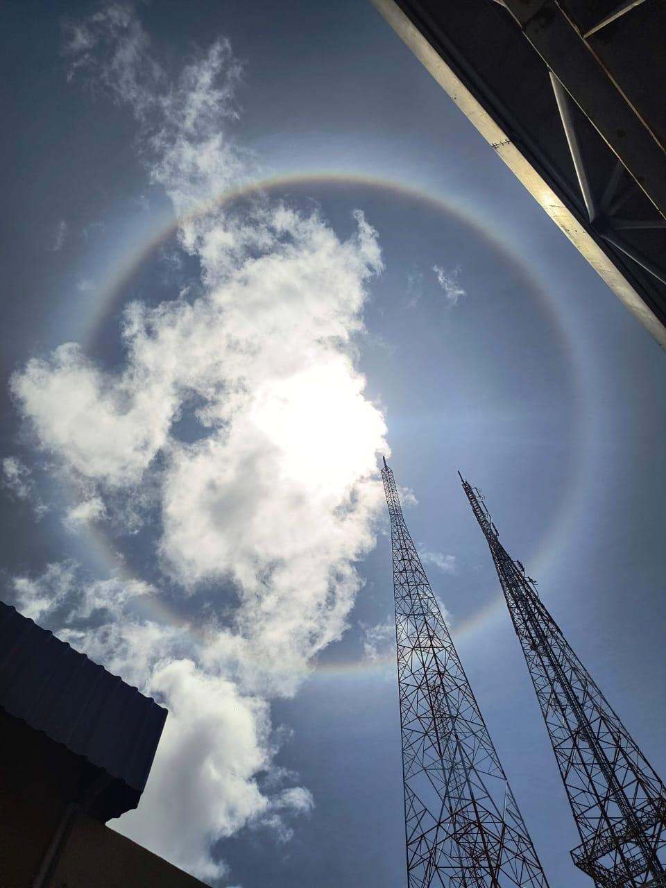 Círculo similar ao arco-íris ao redor do sol, com nuvens ao redor.