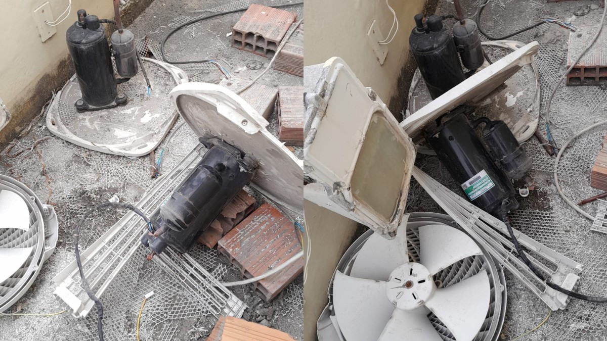 Uma pilha de componentes de ar condicionado desmontados, incluindo compressores pretos, pás de ventilador brancas e detritos variados, espalhados em uma superfície suja.