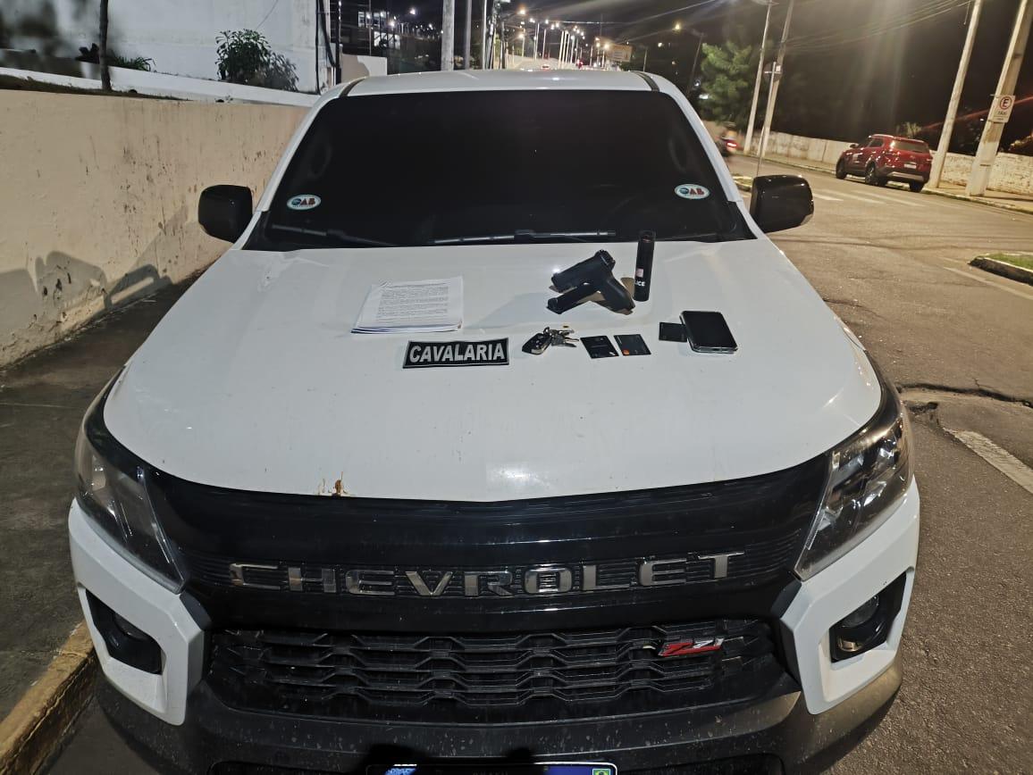 A imagem mostra um carro branco, com adesivos da OAB-CE, e em cima do capô há cartões bancários, uma chave de carro, um celular, um simulacro de arma de fogo e um spray de pimenta.