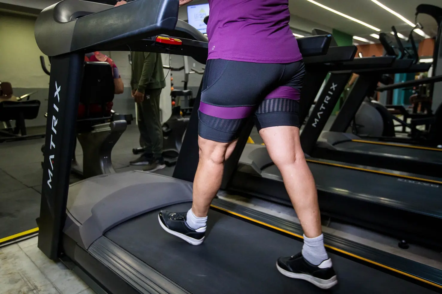 Foto que contém pessoa, provavelmente do sexo feminino, fazendo esteira em academia.