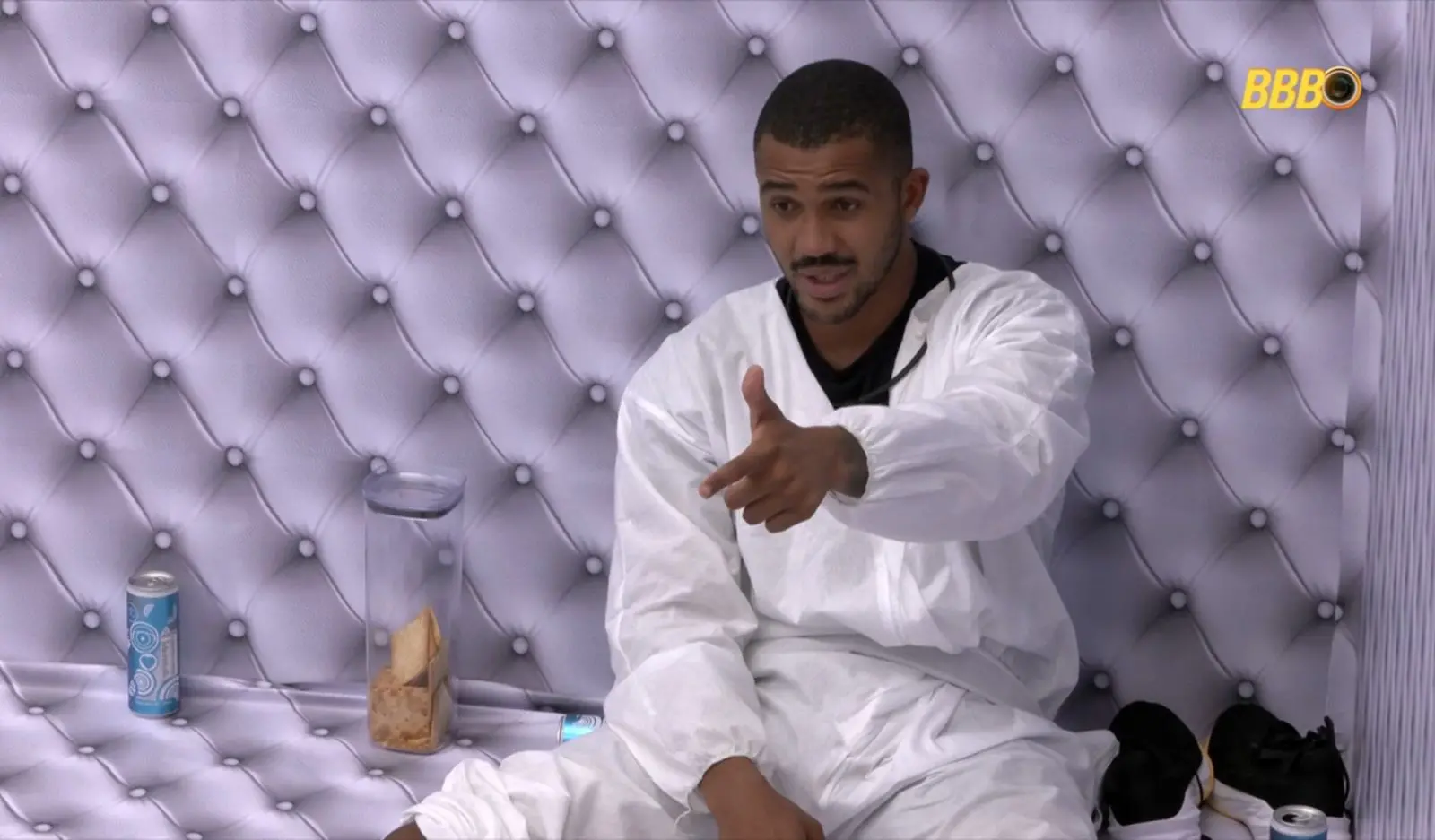 Matheus, participante do BBB, sentado e apontando com o dedo.