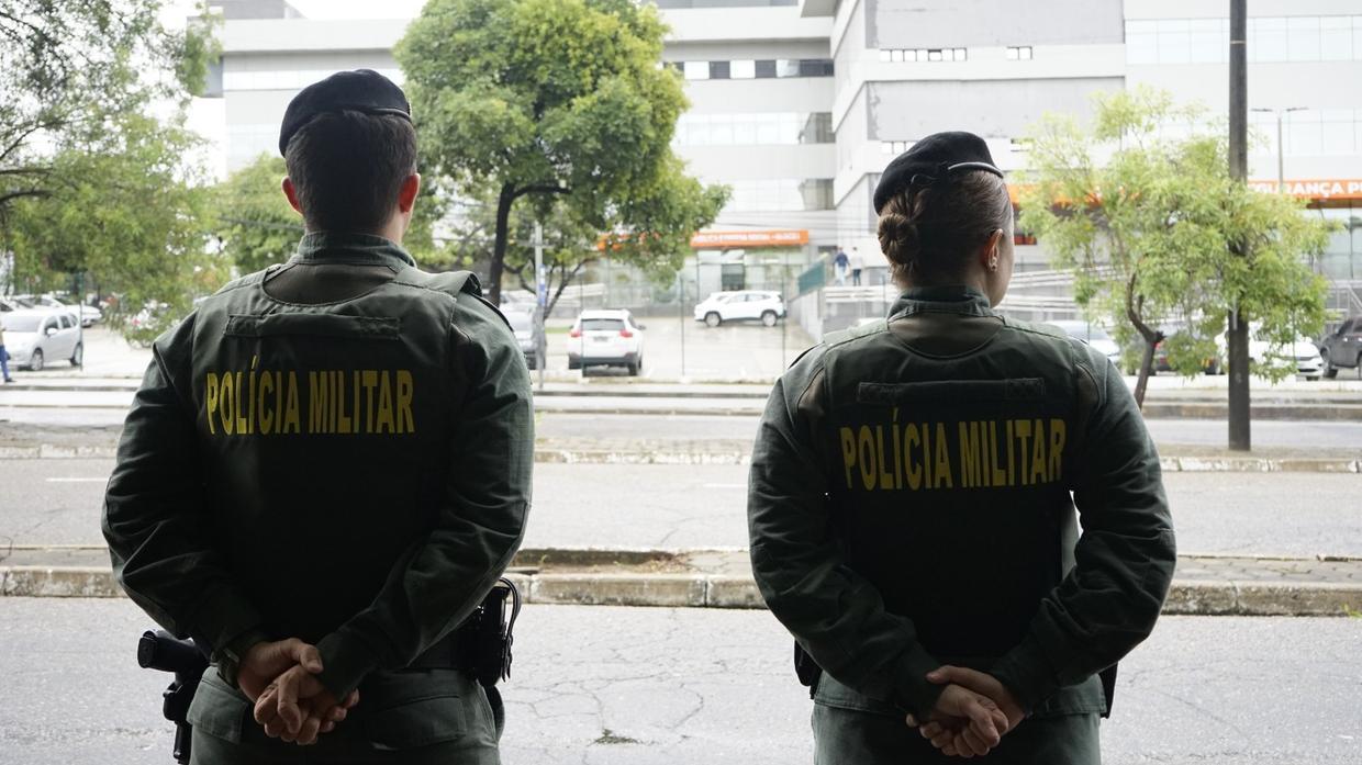 A imagem mostra dois policiais militares, fardados, em frente ao prédio da Secretaria da Segurança Pública e Defesa Social do Ceará.