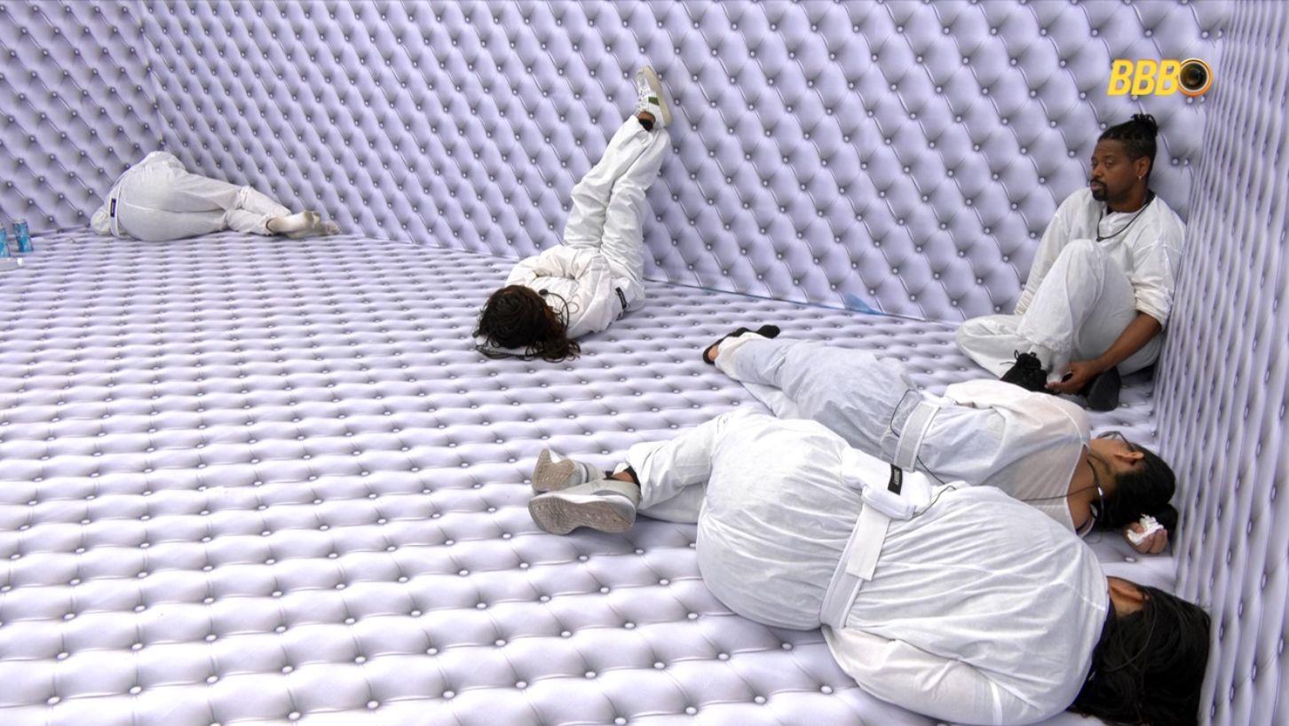 A imagem mostra cinco pessoas de branco, sendo quatro deitadas e uma sentada, no Quarto Branco do reality show BBB 26.