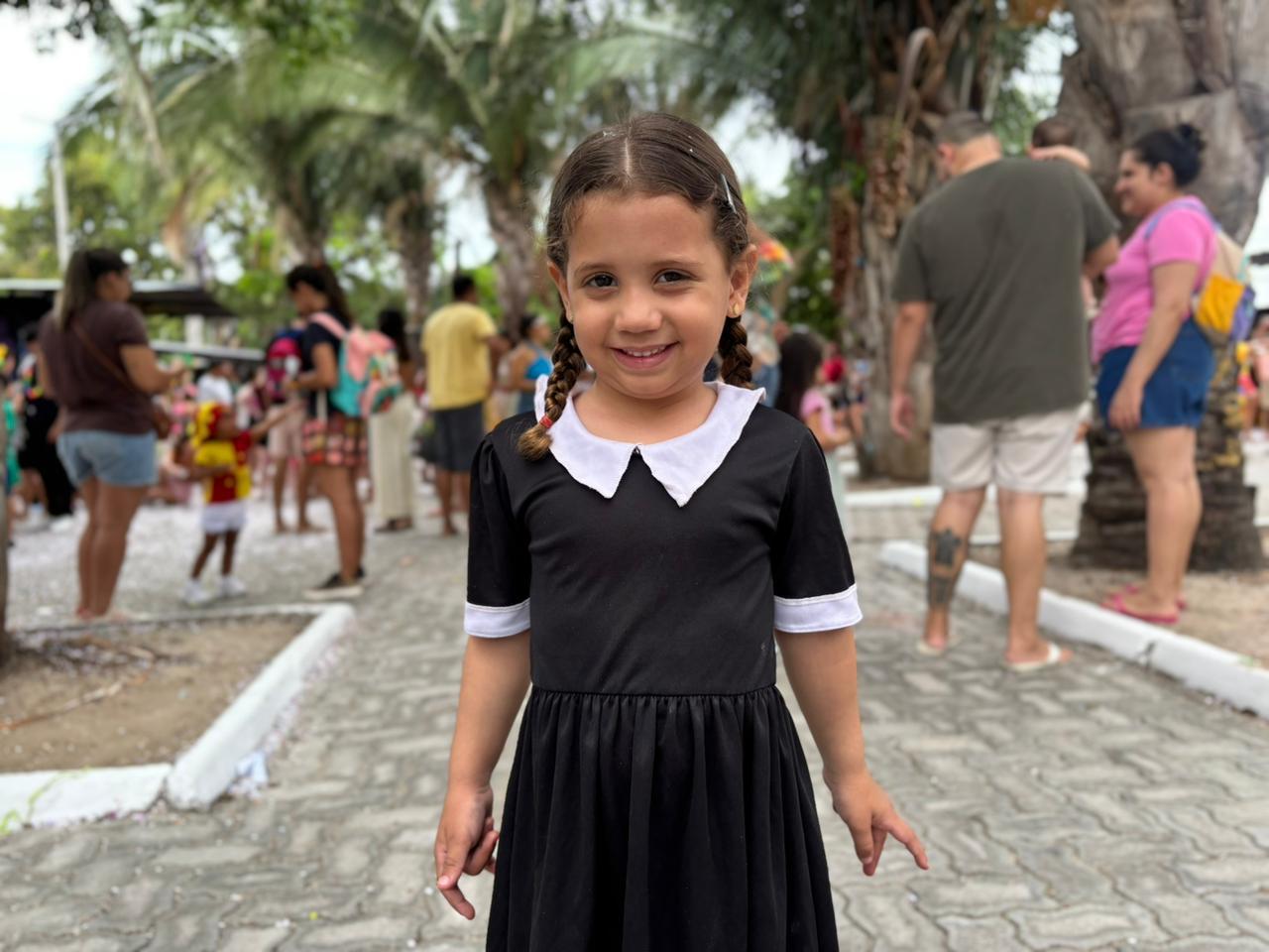 Criança vestida de Wandinha sorri para a câmera.