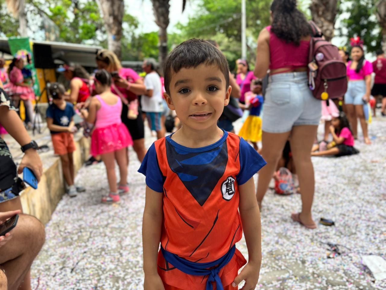 Criança sorri para a câmera em meio a um bloquinho de Carnaval.