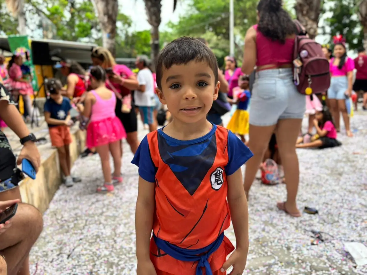 Criança sorri para a câmera em meio a um bloquinho de Carnaval.