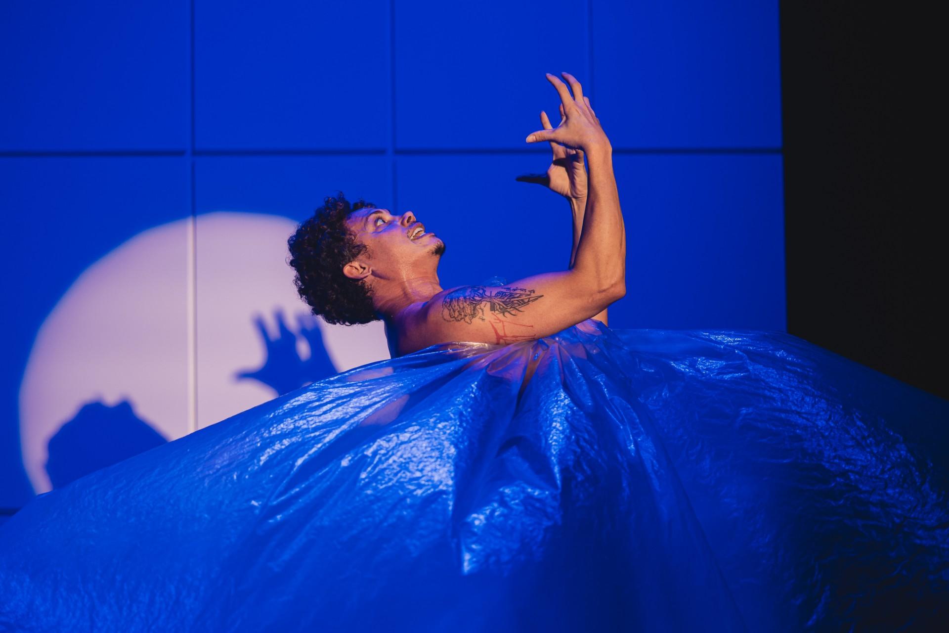 Ator Silvero Pereira em um fundo azul encenando em seu novo espetáculo, “Pequeno Monstro”.