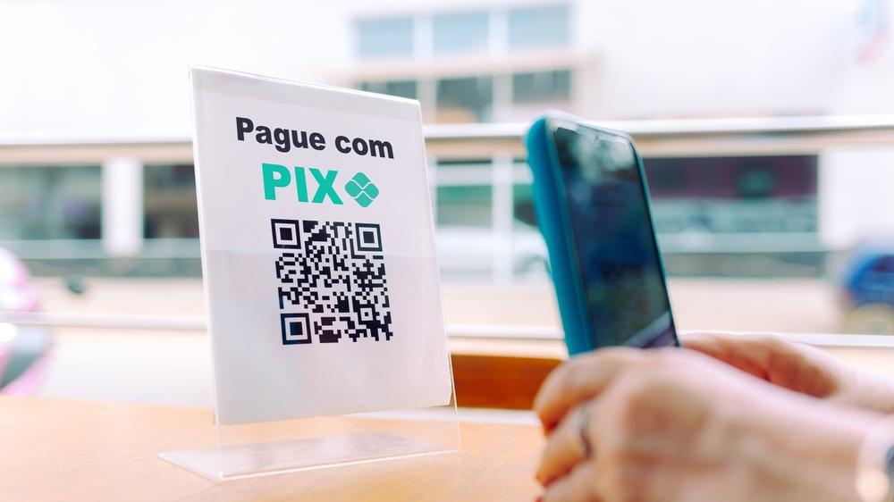 Pessoa fazendo pagamento por pix em celular com capinha azul e em cima de bancada de madeira.