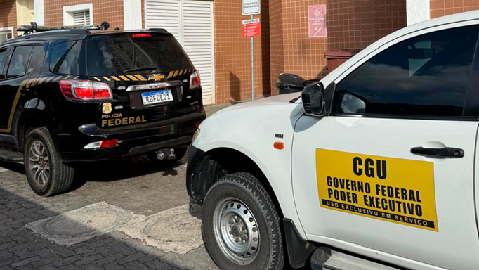 Viaturas da Polícia Federal e da CGU estacionadas lado a lado em frente a um prédio; o carro branco exibe adesivo ‘CGU Governo Federal Poder Executivo’ e o preto identifica a Polícia Federal.
