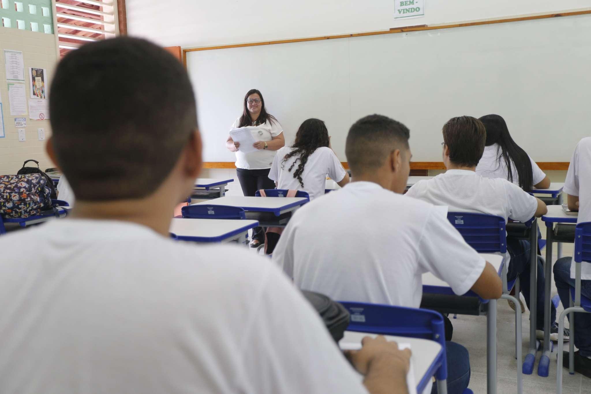 Foto mostra sala de aula com professora ao fundo e estudantes nas carteiras em escola no Ceará.