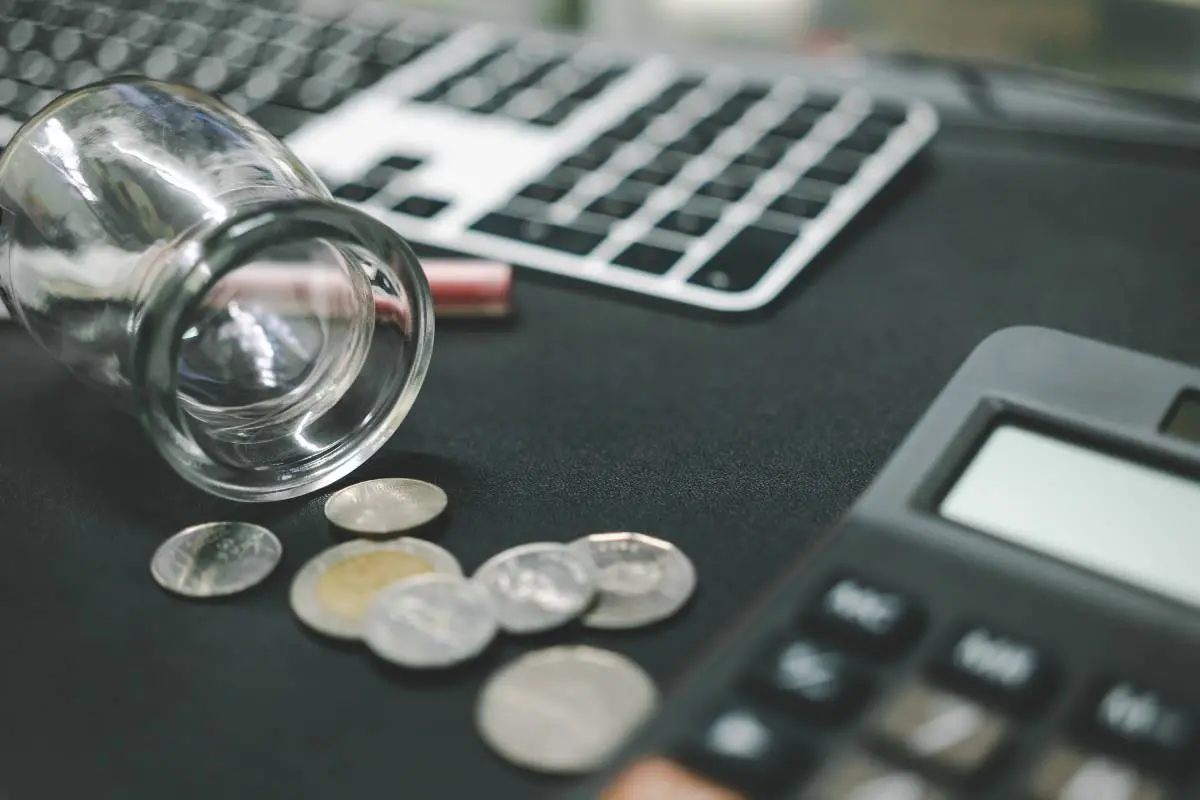 Imagem mostra moedas e calculadoras sobre uma mesa.