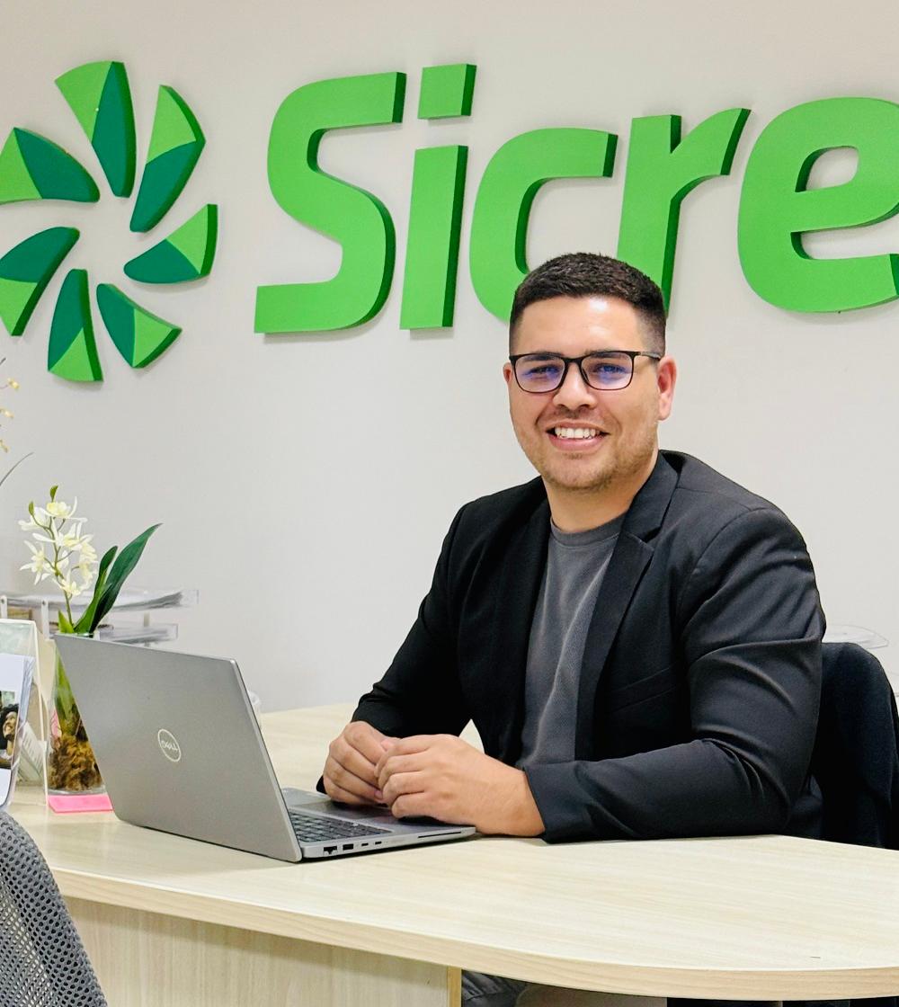 Homem sorridente sentado à mesa em ambiente corporativo do Sicredi, representando o uso consciente do crédito e planejamento financeiro