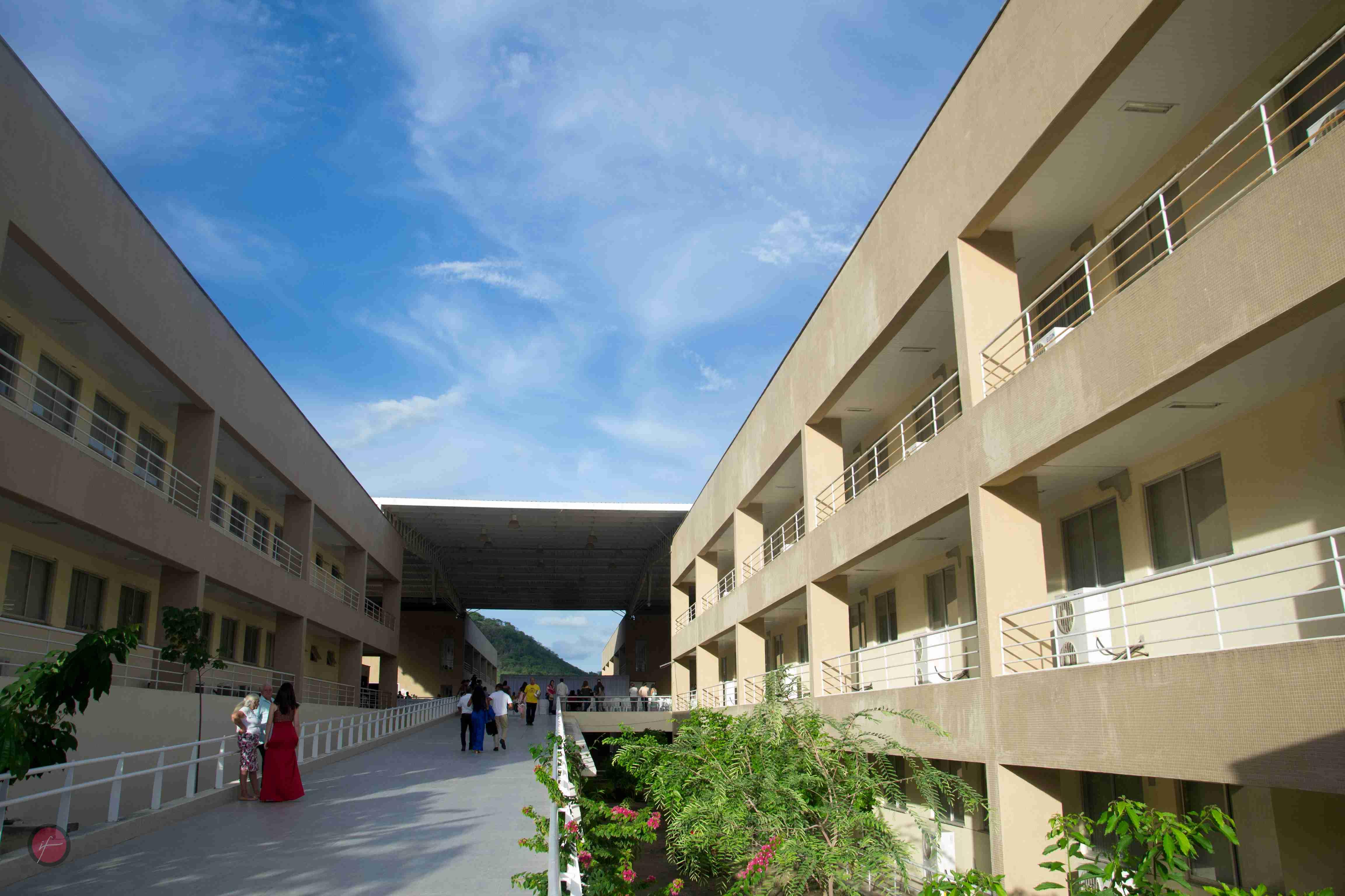 Vista de uma passarela elevada conectando construções cor de areia, com montanhas e vegetação no horizonte na Unilab em Redenção, no Ceará.
