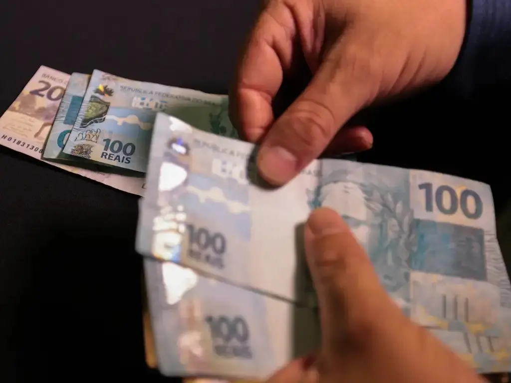 Pessoa contando dinheiro, em notas de R$ 100.