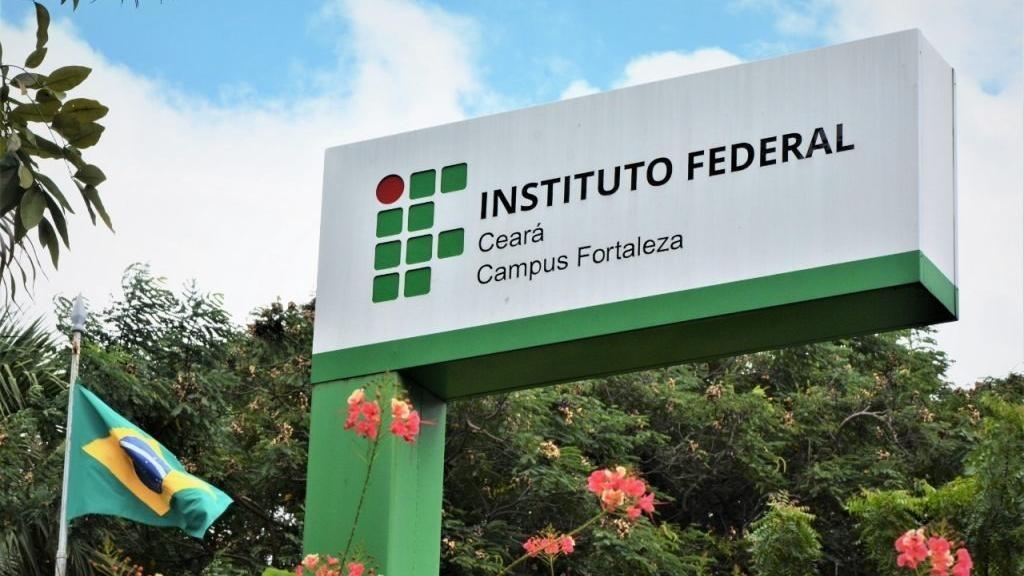 Fachada do campus do IFCE em Fortaleza, com placa com nome da instituição e, abaixo, vegetação e flores.