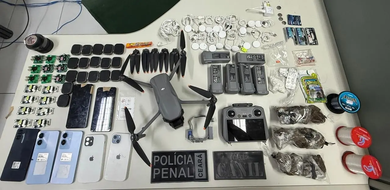 A imagem mostra diversos materiais apreendidos com criminosos, como um drone, celulares, relógios com aplicativos, drogas e outros equipamentos, em cima de uma mesa.
