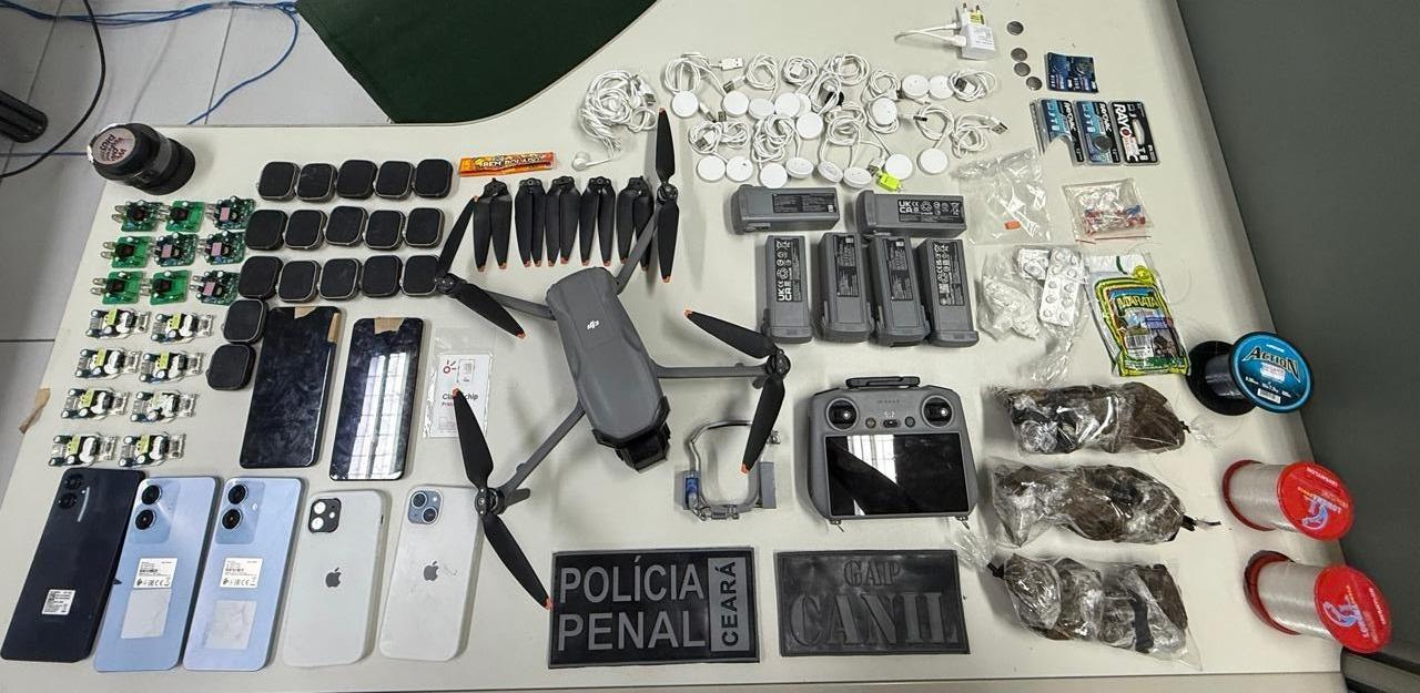 A imagem mostra diversos materiais apreendidos com criminosos, como um drone, celulares, relógios com aplicativos, drogas e outros equipamentos, em cima de uma mesa.