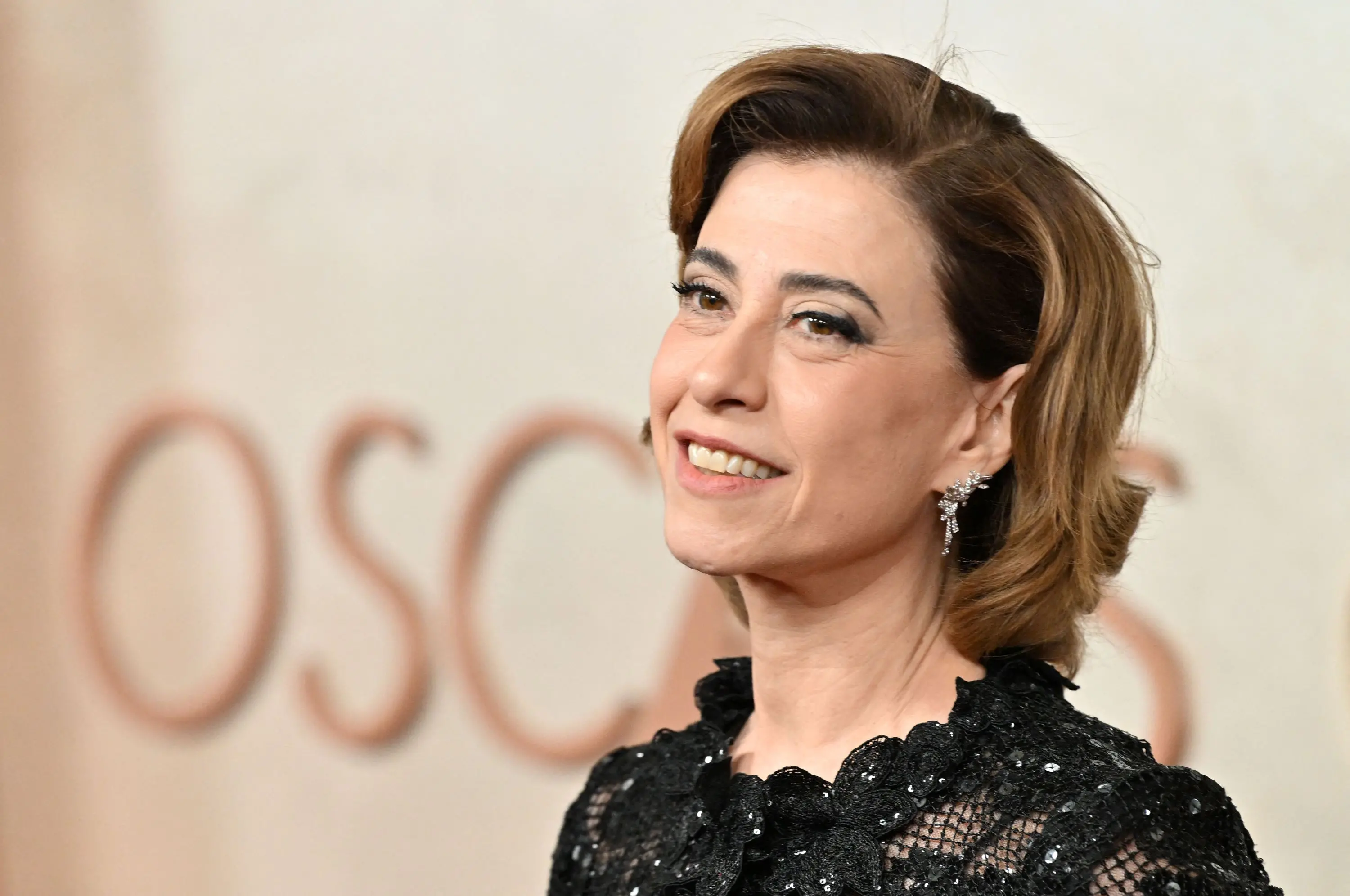 atriz fernanda torres diante de uma parede em tons claros com a palavra OSCARS.