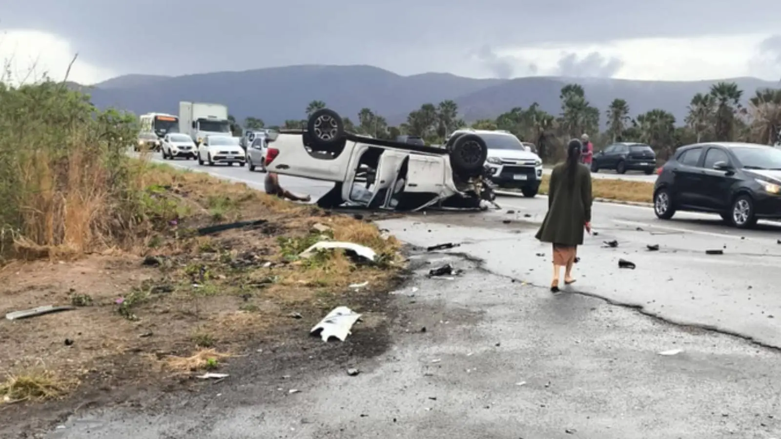 Imagem mostra cena de acidente em rodovia com uma caminhonete branca capotada no acostamento da CE-085, em Caucaia, com detritos espalhados e tráfego lento ao fundo.