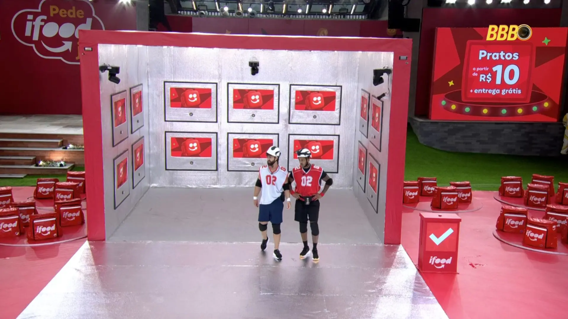 Cena interna do BBB mostrando diversos confinados sentados em um sofá e no chão, em um ambiente decorado com espelhos e itens de luxo.