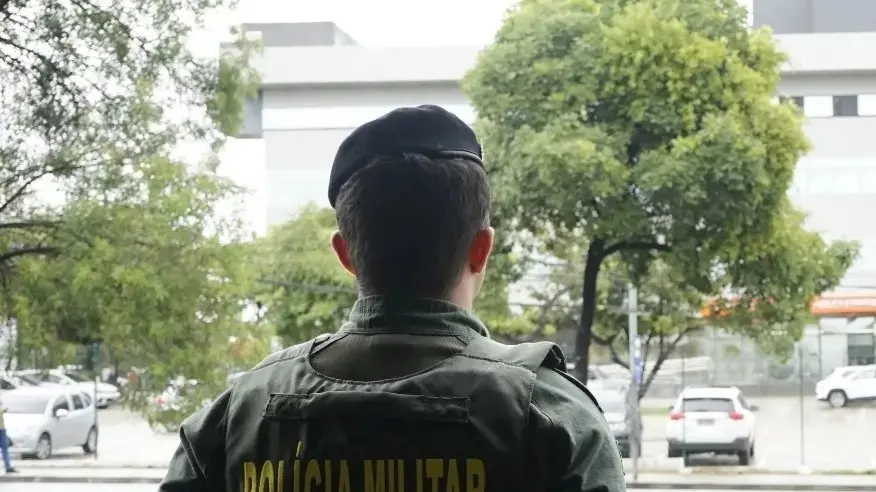 A imagem mostra um policial militar fardado, de costas, de frente para prédio da SSPDS.
