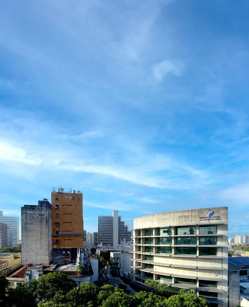 Vista urbana com prédios no centro de Fortaleza; à direita, o edifício moderno do Tribunal de Contas do Estado do Ceará, sob céu azul com poucas nuvens.