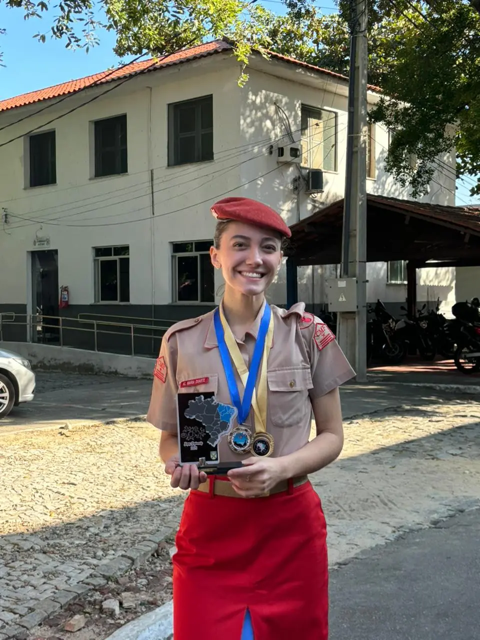 Imagem mostra a ex-estudante do Colégio Militar de Fortaleza, Maria Letícia Duarte, segurando troféu e usando medalhas que recebeu na instituição de ensino.