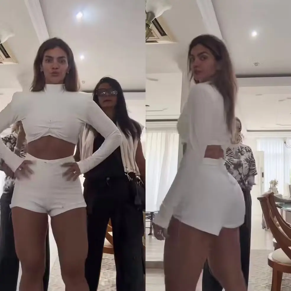 Foto de Kelly Key, antes da festa do BBB26. Ela está de cropped branco, com um short também branco olhando para um espelho.